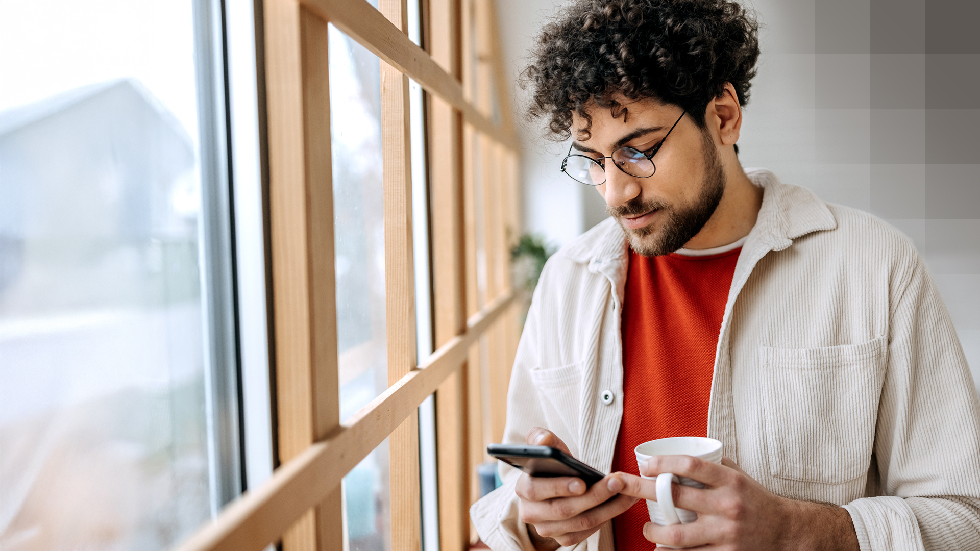 Un jeune homme tient une tasse à la main et regarde son smartphone tout en se renseignant sur le modèle Medi, Win.Easy.